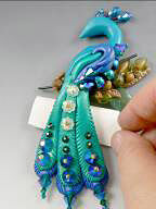 Clay peacock with folded paper under tail feathers